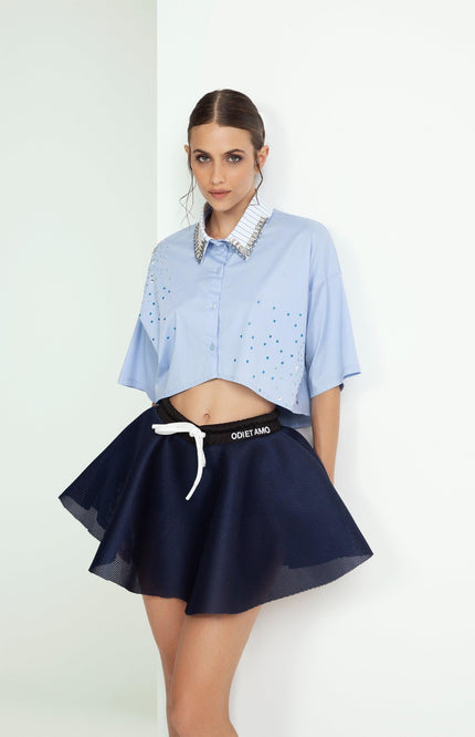Woman models blue embellished cropped shirt and flared navy mini skirt, modern fashion look