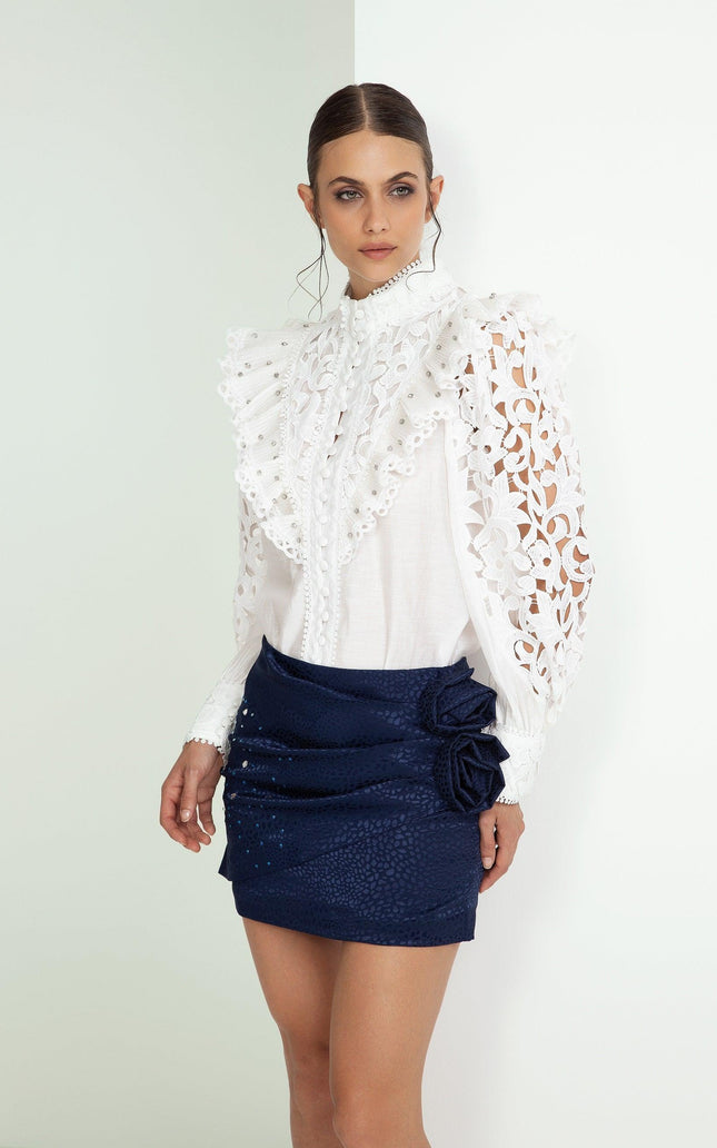 Woman in white ruffled lace blouse and navy blue mini skirt with floral detail, fashion look