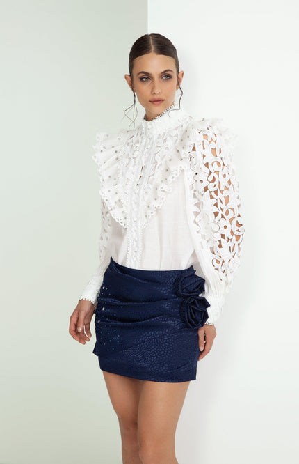 Woman in white ruffled lace blouse and navy blue mini skirt with floral detail, fashion look