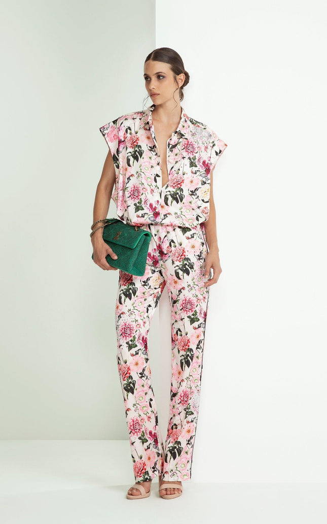 Woman wearing a pink floral blouse and pants set, holding a green clutch bag