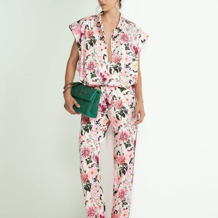 Woman wearing a pink floral blouse and pants set, holding a green clutch bag