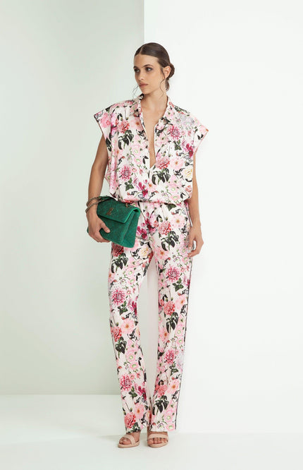 Woman wearing a pink floral blouse and pants set, holding a green clutch bag