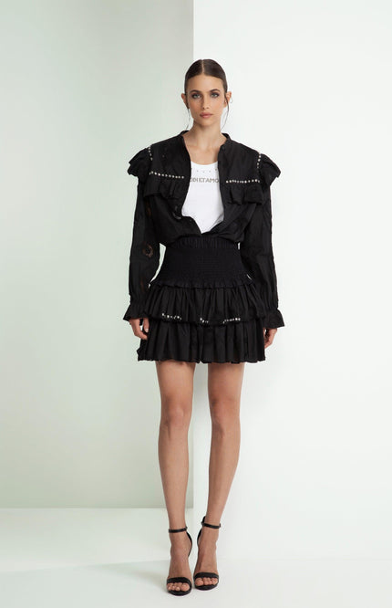 Woman in black ruffled mini skirt, white graphic tee, and black studded jacket