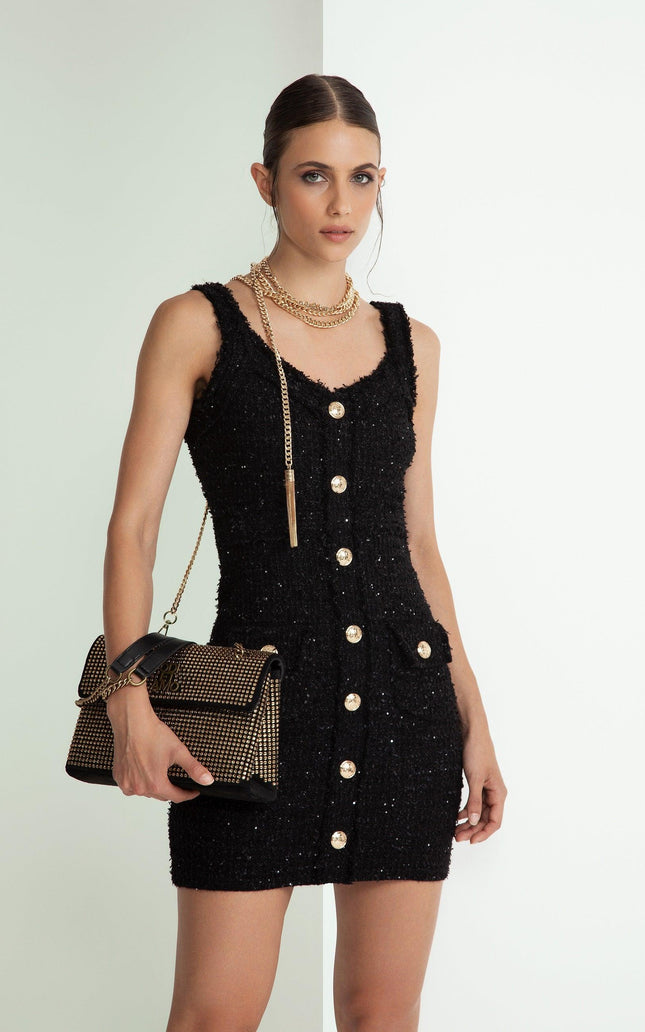 Woman in black sleeveless button-down mini dress with gold chain accessories and studded handbag