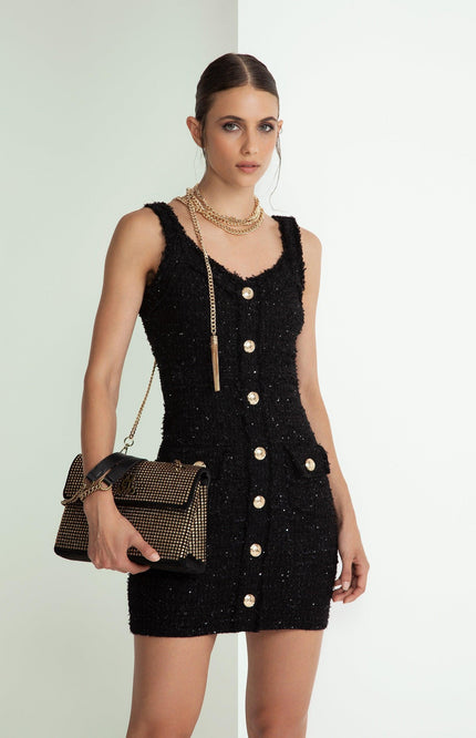 Woman in black sleeveless button-down mini dress with gold chain accessories and studded handbag