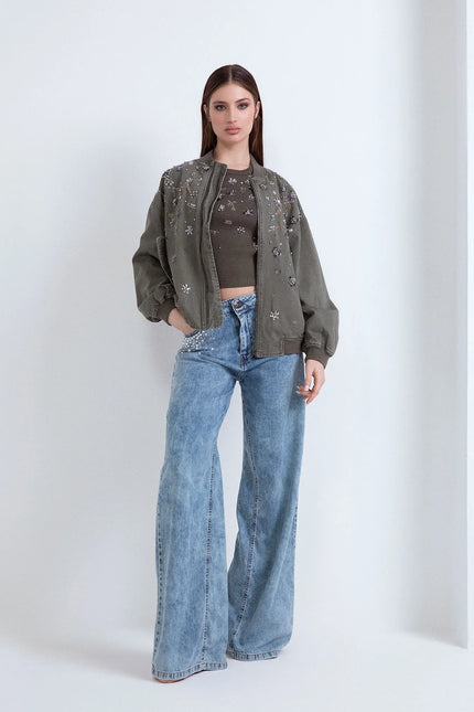 Donna con bomber verde decorato, top grigio e jeans a gamba larga su sfondo bianco