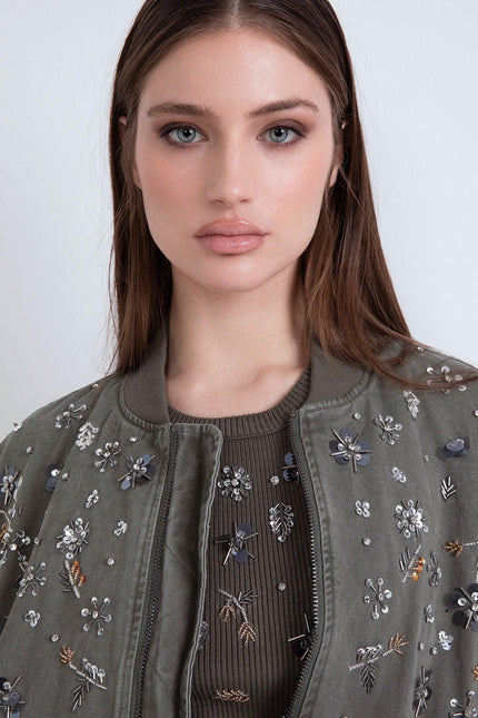 Primo piano di una donna con bomber verde militare ricamato con fiori di paillettes e strass.