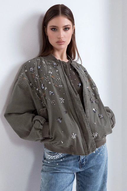 Donna con bomber verde militare decorato da strass floreali e jeans chiari con borchie.