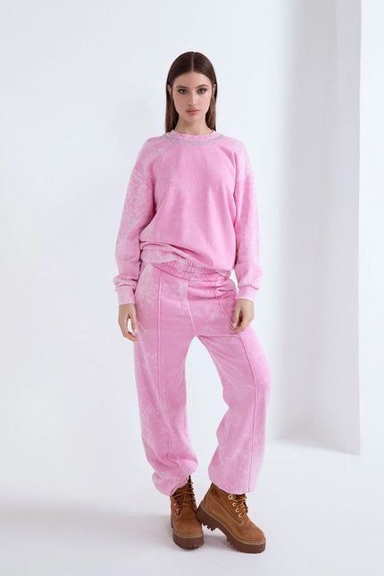 Modella in tuta rosa effetto lavato con felpa a girocollo decorata e scarponcini scamosciati.