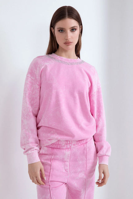 Modella con capelli castani lisci in felpa di cotone rosa effetto lavato con borchie sullo scollo.