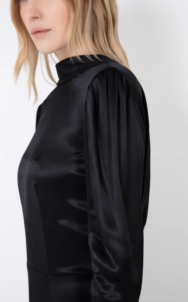 Woman wearing long sleeve black satin dress with gathered shoulders and high neckline