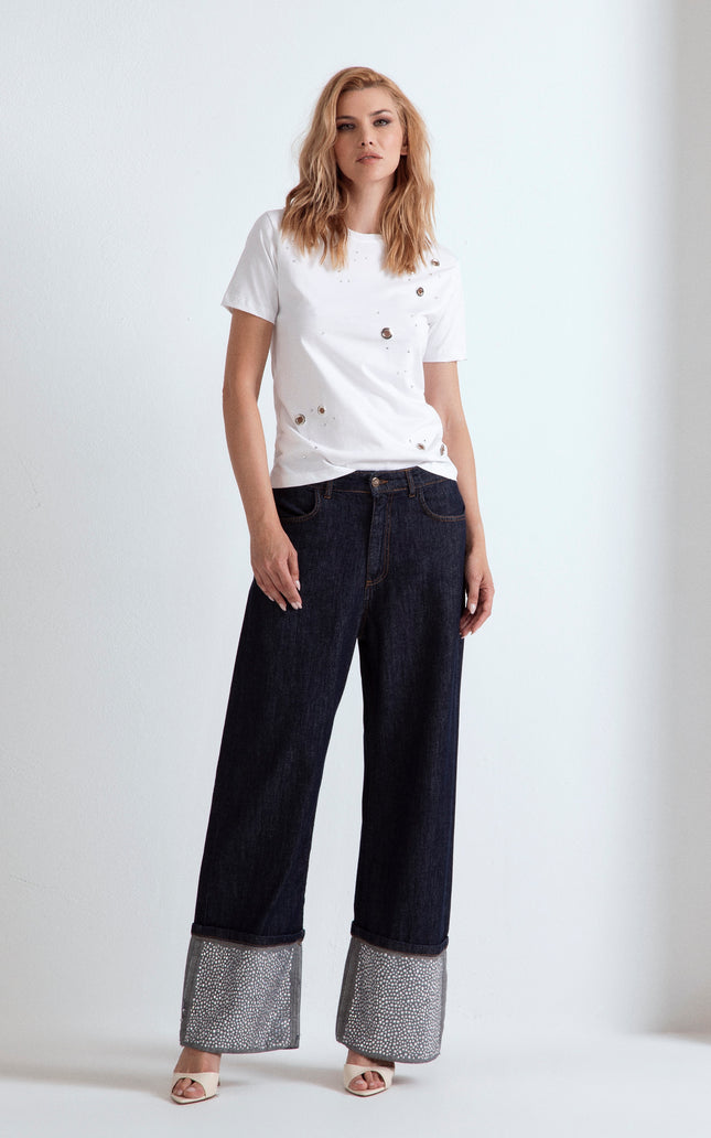 Modella con t-shirt bianca ODI ET AMO con strass e jeans a gamba larga con risvolto.