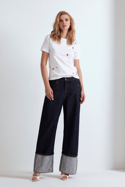 Modella con t-shirt bianca ODI ET AMO con strass e jeans a gamba larga con risvolto.