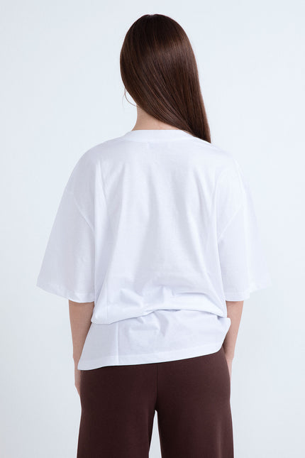 Retro di t-shirt donna bianca oversize a maniche corte con capelli lunghi castani e pantaloni marroni