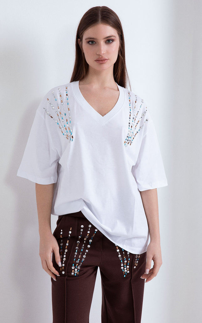 T-shirt donna bianca oversize con scollo a V e applicazioni di pietre colorate sulle spalle abbinata a pantaloni marroni