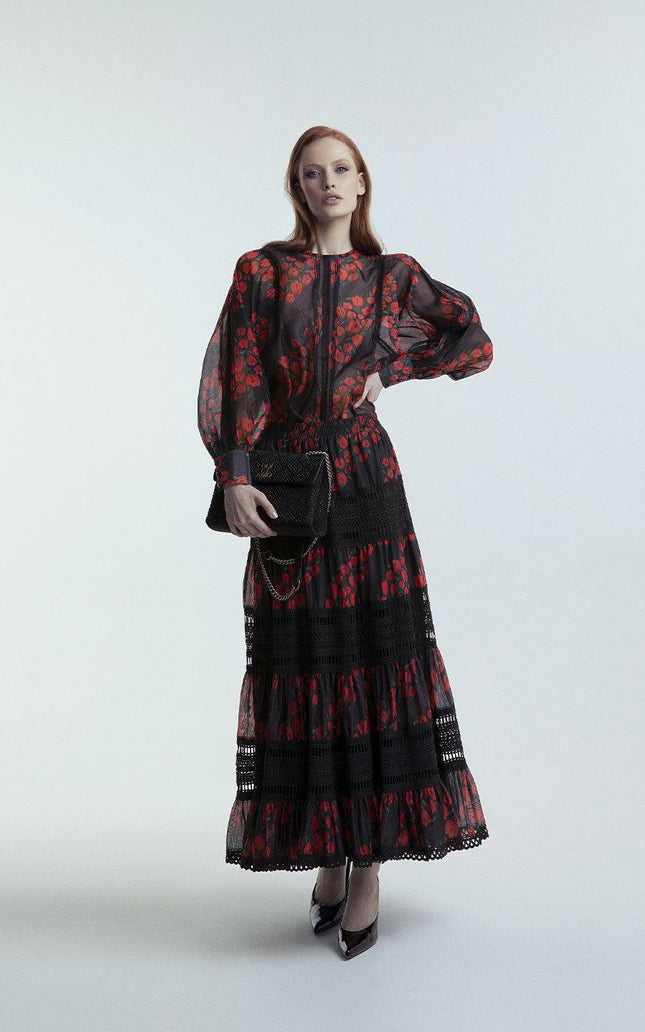 Woman in sheer black and red floral maxi dress holding black clutch, fashion photoshoot