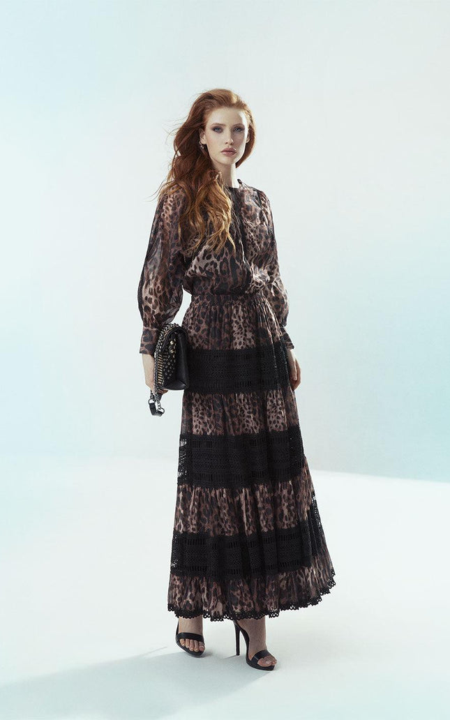 Woman in leopard print maxi dress with lace panels, holding a black studded bag