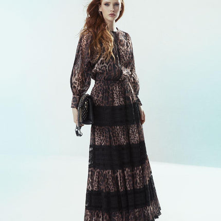 Woman in leopard print maxi dress with lace panels, holding a black studded bag