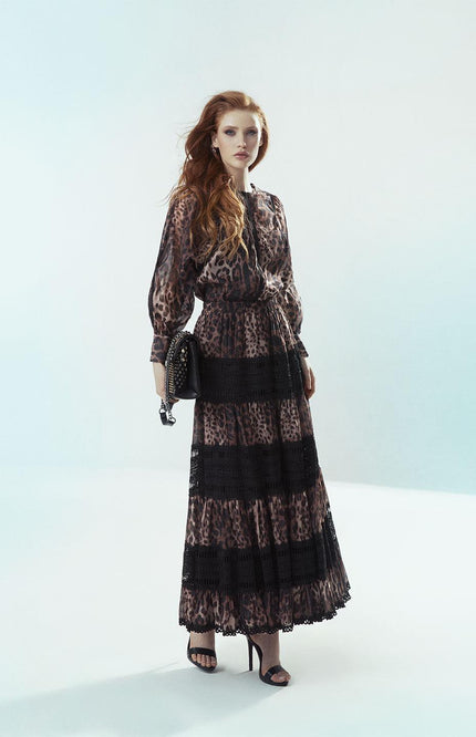 Woman in leopard print maxi dress with lace panels, holding a black studded bag