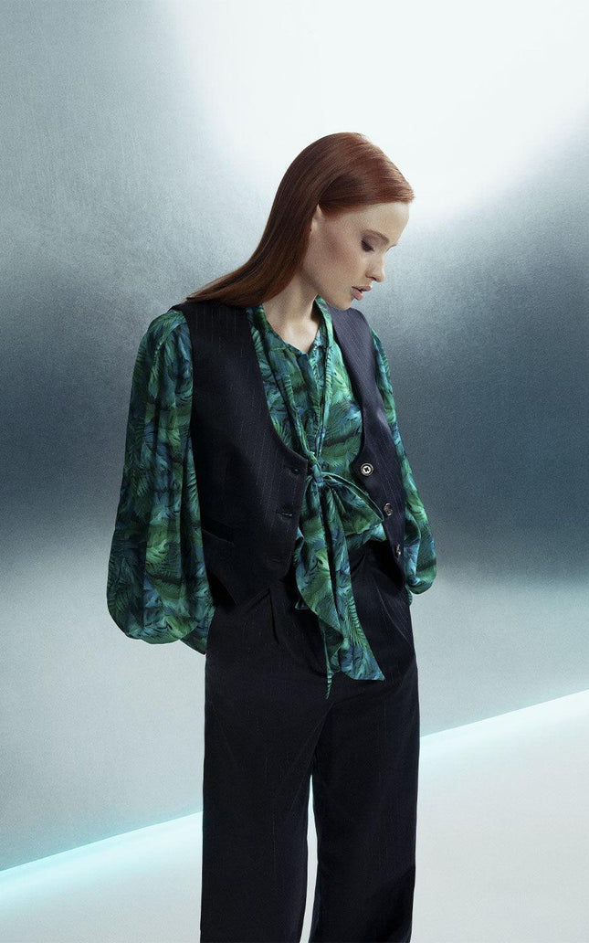 Woman in green patterned blouse and black vest with wide-leg pants, stylish fashion look