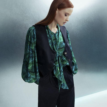 Woman in green patterned blouse and black vest with wide-leg pants, stylish fashion look