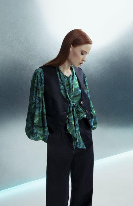 Woman in green patterned blouse and black vest with wide-leg pants, stylish fashion look