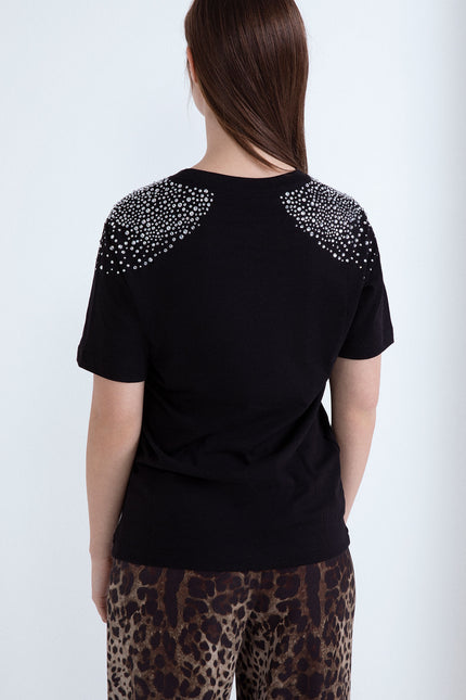 Vista posteriore di una t-shirt nera da donna con applicazione di strass brillanti sulle spalle.